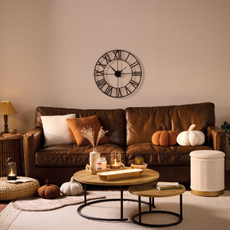 Bown sofa with pumpkin cushions. In front is a round coffe table featuring candles and a diffuser