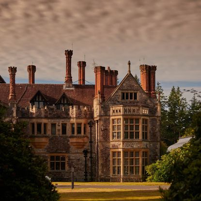 Rhinefield House Hotel with clouds in the background and trees lining the sides