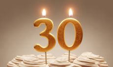 30th birthday or anniversary celebration. Lit golden number candles on cake with icing in neutral tones. 