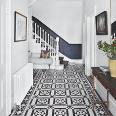 White painted hallway with black and white tiled floor, a white radiator on the wall, and a staircase