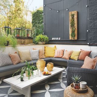 Outdoor seating area with black rattan furniture and cushions on tiled patio with wooden wall planter with plants