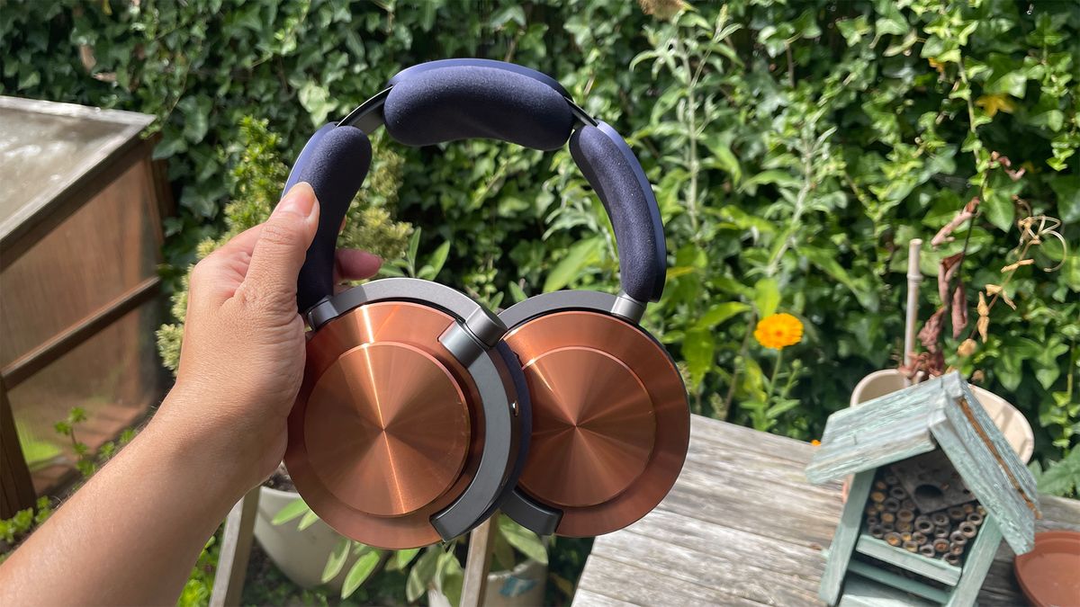 Dyson OnTrac wireless headphones in hand with garden hedge in background