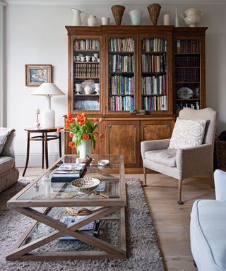 An old wooden dresser full of books sits against the wall of a living room with a neutral, rustic scheme.