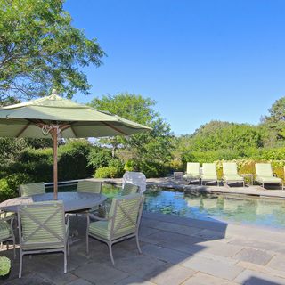 A paved patio with garden table and chairs set beside a swimming pool