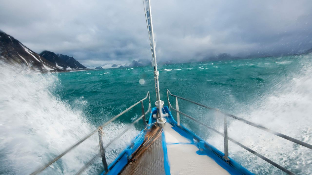 A sailboat crashes through rough seas.