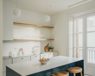 Minimalist small kitchen ideas featuring white shelves, island, wooden accents and open shelving with only clear glass tableware on
