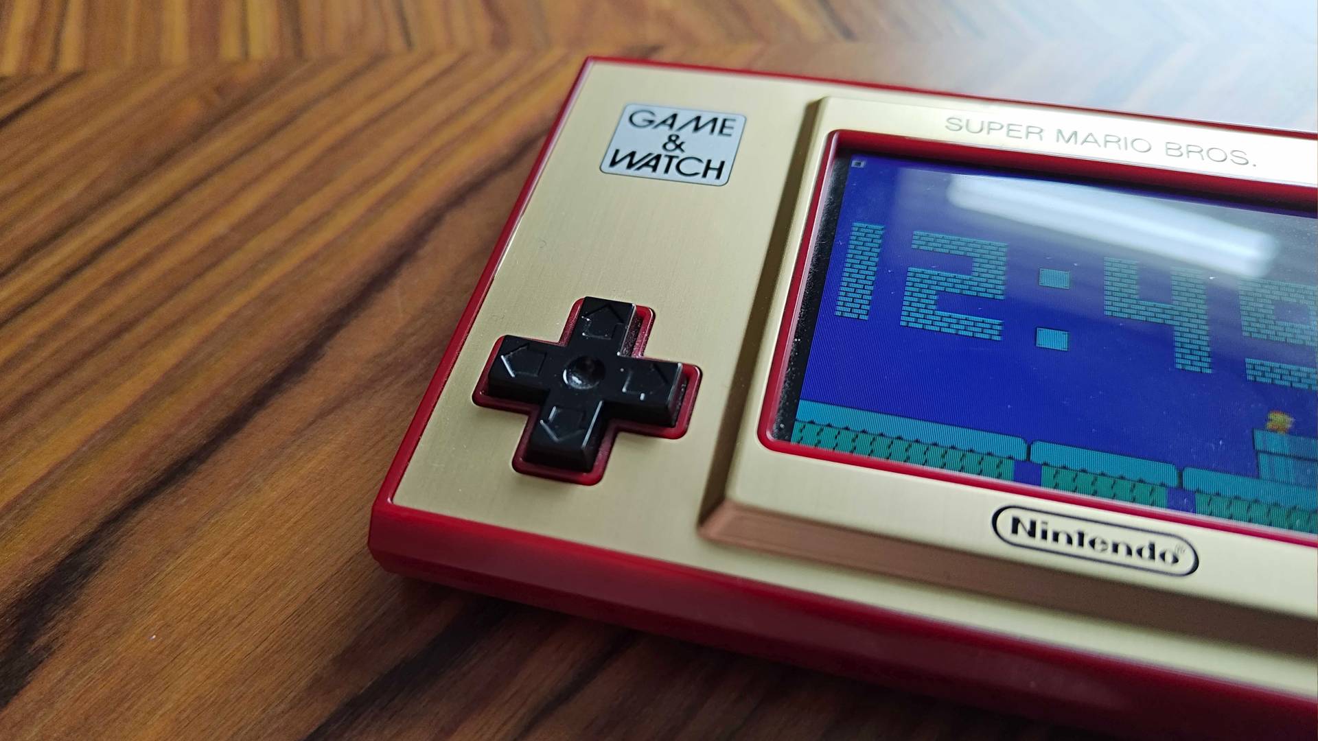 Close up of Mario Game and Watch d-pad sitting on woodgrain desk.