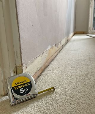 A measuring tape leaning against the base of a wall with no baseboards fitted