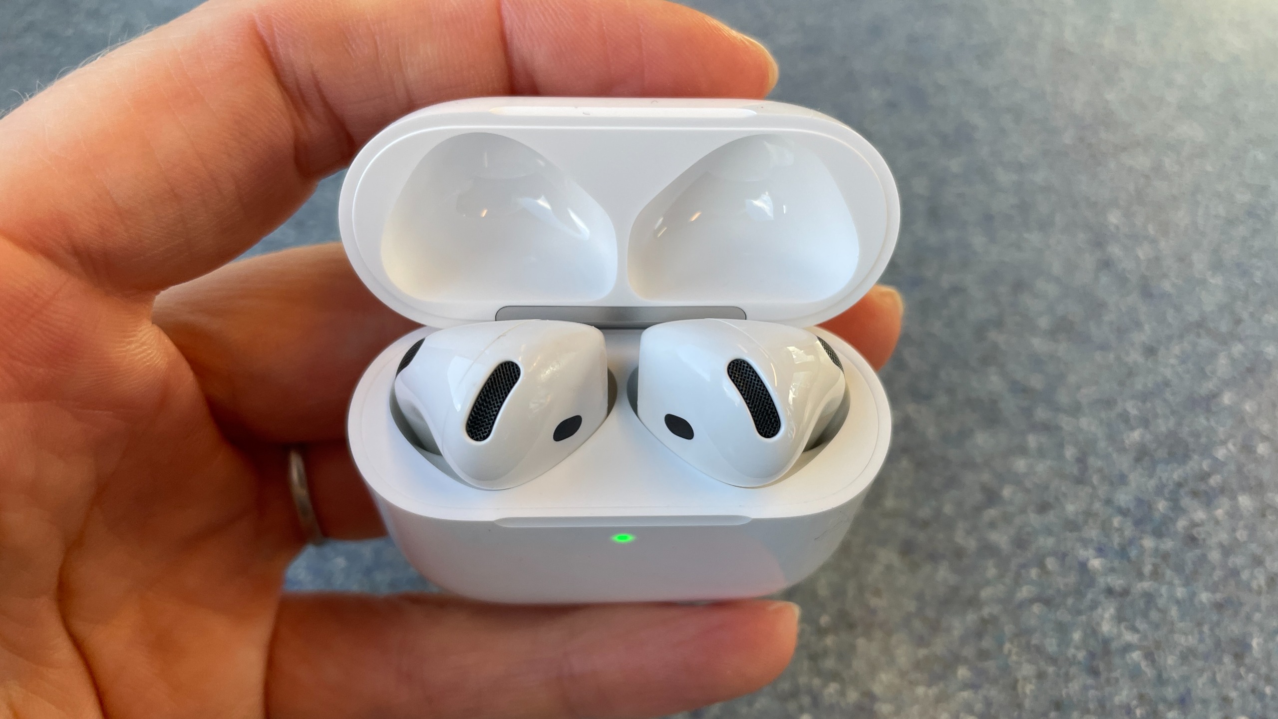 Apple AirPods 5 with Wireless Charging, on a blue table and held in a hand