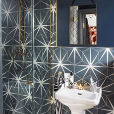 a bathroom with Lilypad bathroom tile design of blue hexagons with white stars, a white vanity with gold taps, a glass shower and mirror with gold trimmings