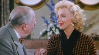Marilyn Monroe sits smiling as an old man holds her hand in Gentlemen Prefer Blondes.