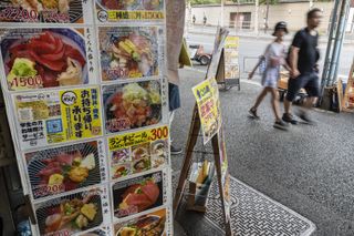 People walk past a sign advertising fresh sushi and Japanese food at the Tsukiji outer fish market in Tokyo.