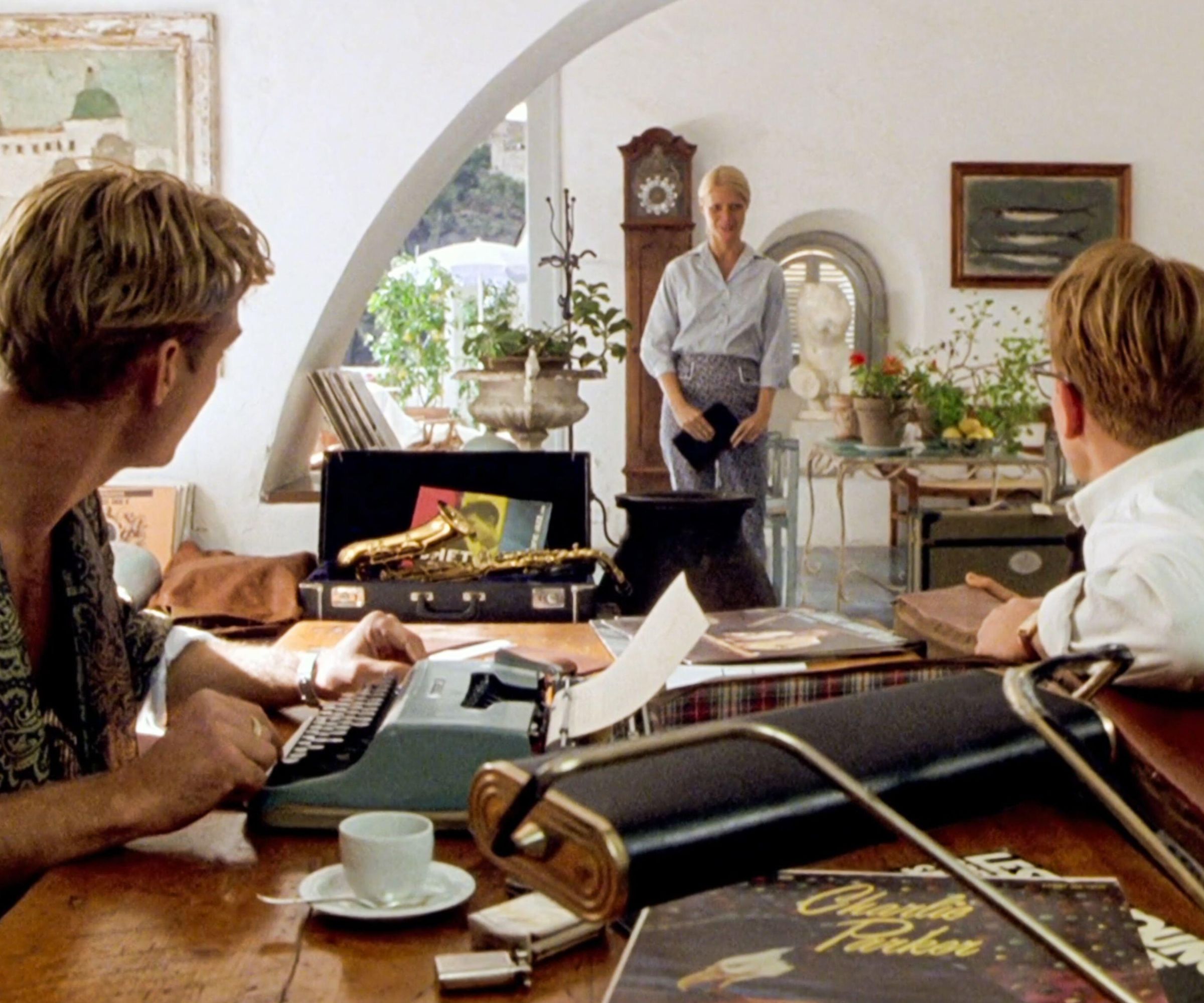 Jude Law, Matt Damon and Gwyneth Paltrow in a living room with curved arch and wood desk and large clock