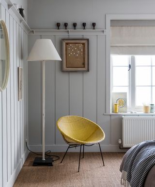 bedroom with high level narrow shelf and hooks, floor lamp, yellow chair and sisal carpet