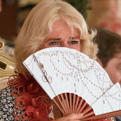 Queen Camilla crying behind a fan while wearing a floral dress during visit to Samoa on October 26, 2024