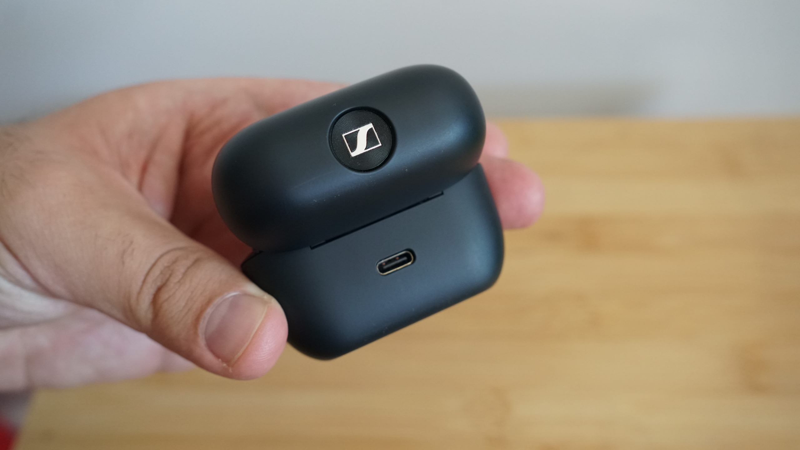 Sennheiser's Accentum Clip held in a hand, over a wooden table, with the case visible