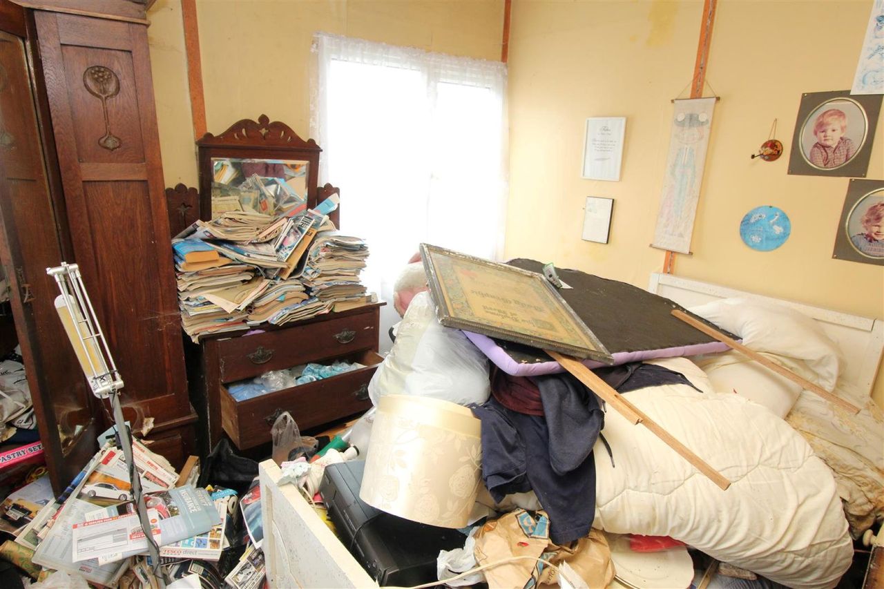 The master bedroom has book and magazines piled on top of cupboards and the bed is covered in picture frames and a wooden stand