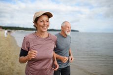 Active senior couple runners jogging outdoors on sandy beach by sea in early morning