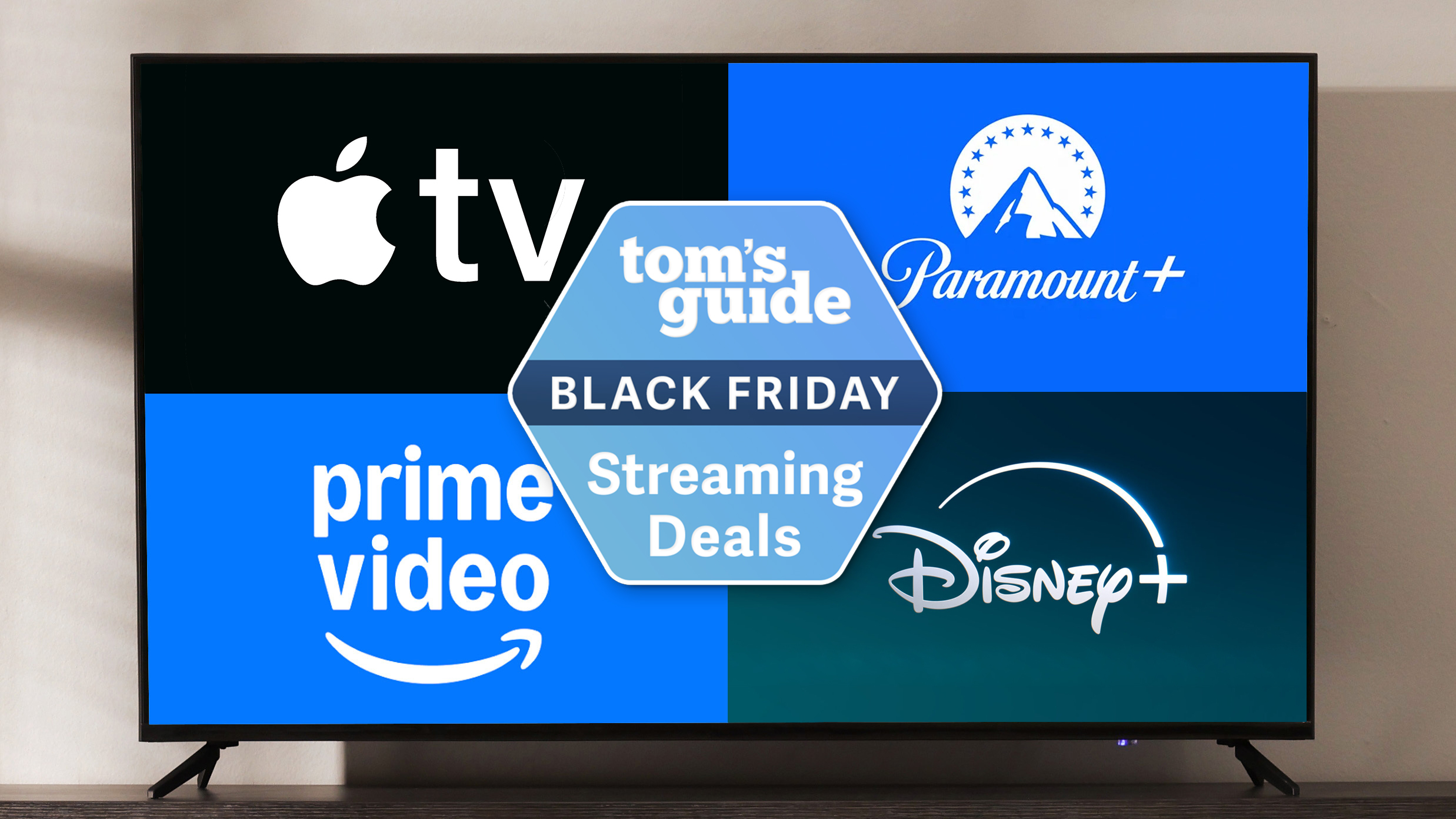 A TV on a stand displaying logos for Apple TV, Paramount Plus, Prime Video and Disney Plus around a Tom&#039;s Guide Black Friday streaming deals badge