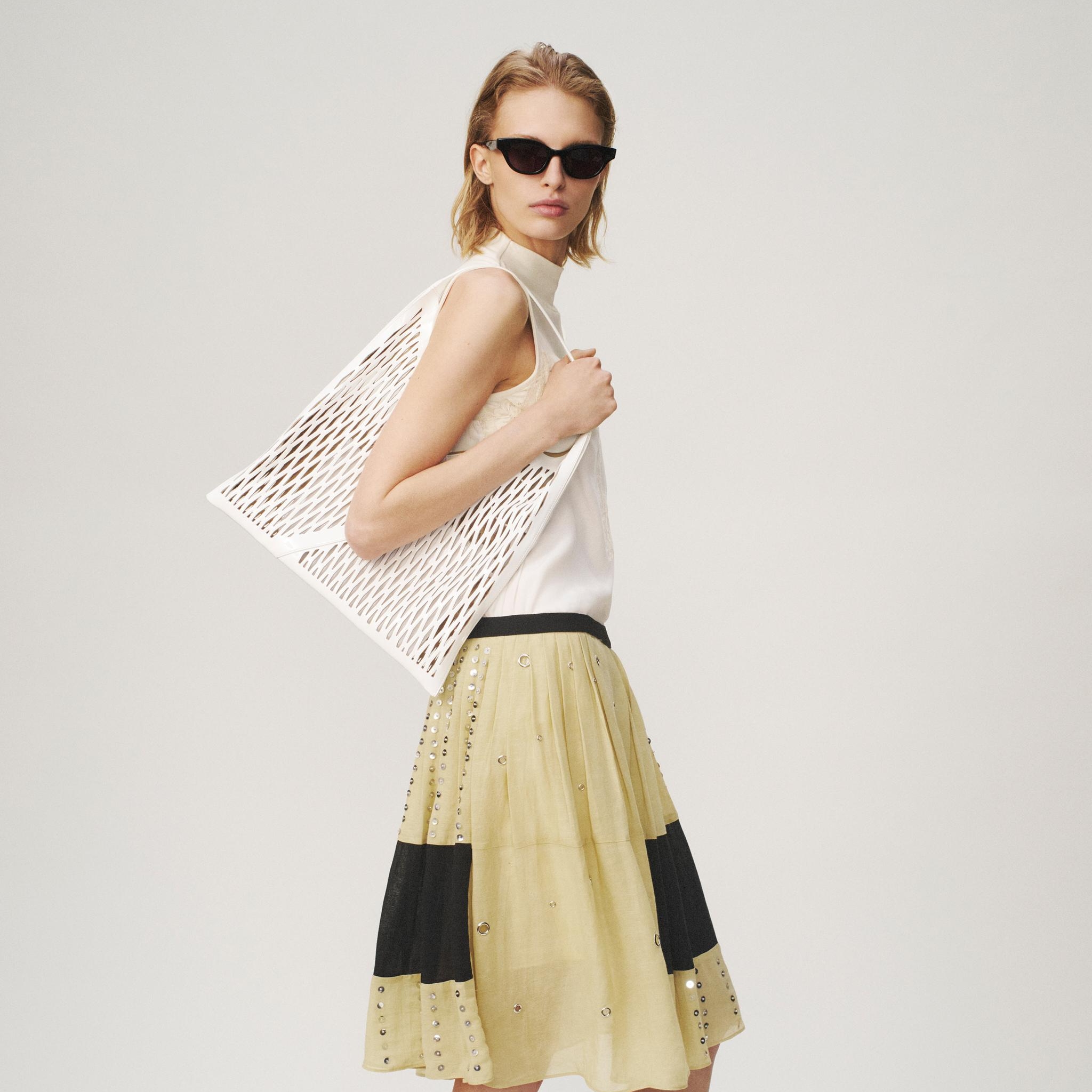 woman holding woven bag in beaded skirt