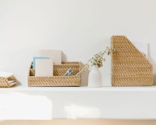 KonMari tidied shelf with wicker storage solutions showing neatly stored notebooks, pens and folders