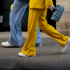 two people walking wearing blue and yellow pants, white sneakers, and a blue handbag