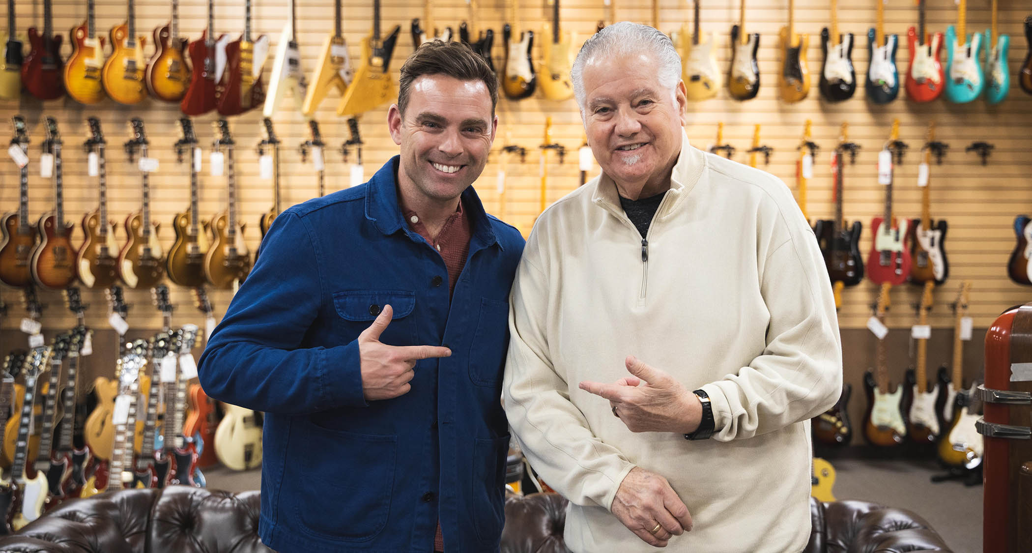 TNAG Global founder/CEO Ben Montague [left] and Norman Harris [right] point to each other as they are photographed on the shop floor at Norman's Rare Guitars.