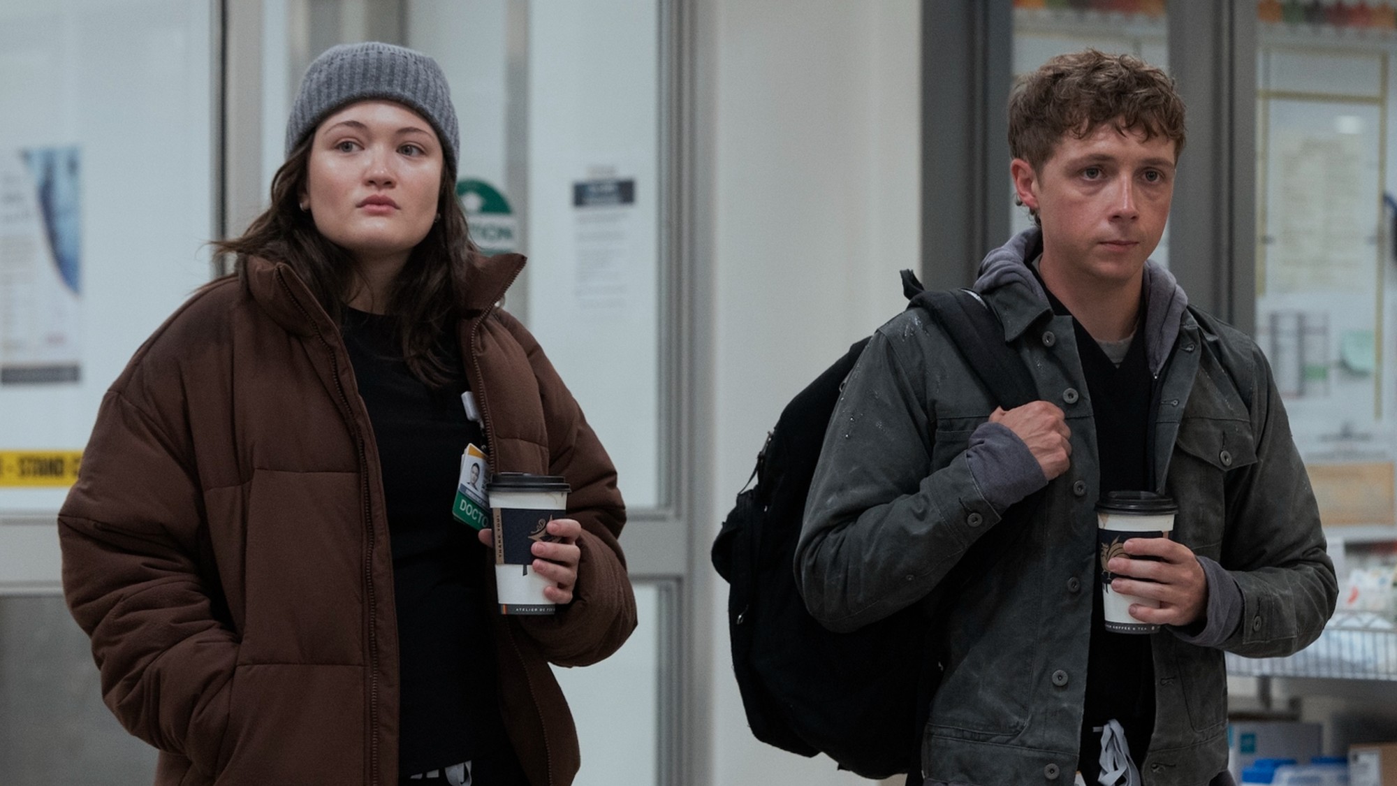 From left to right: Santos and Whitaker waslking into The Pitt holding coffees in their right hands. 