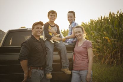 A family of four relaxes on the tailgate of their pickup truck.