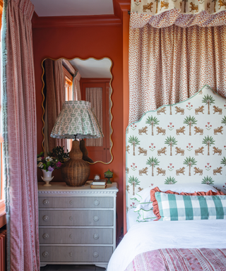 bedrrom designed with lots of patterned fabric with orange walls including leopord print ottoman and rattan lampshade and bedside table