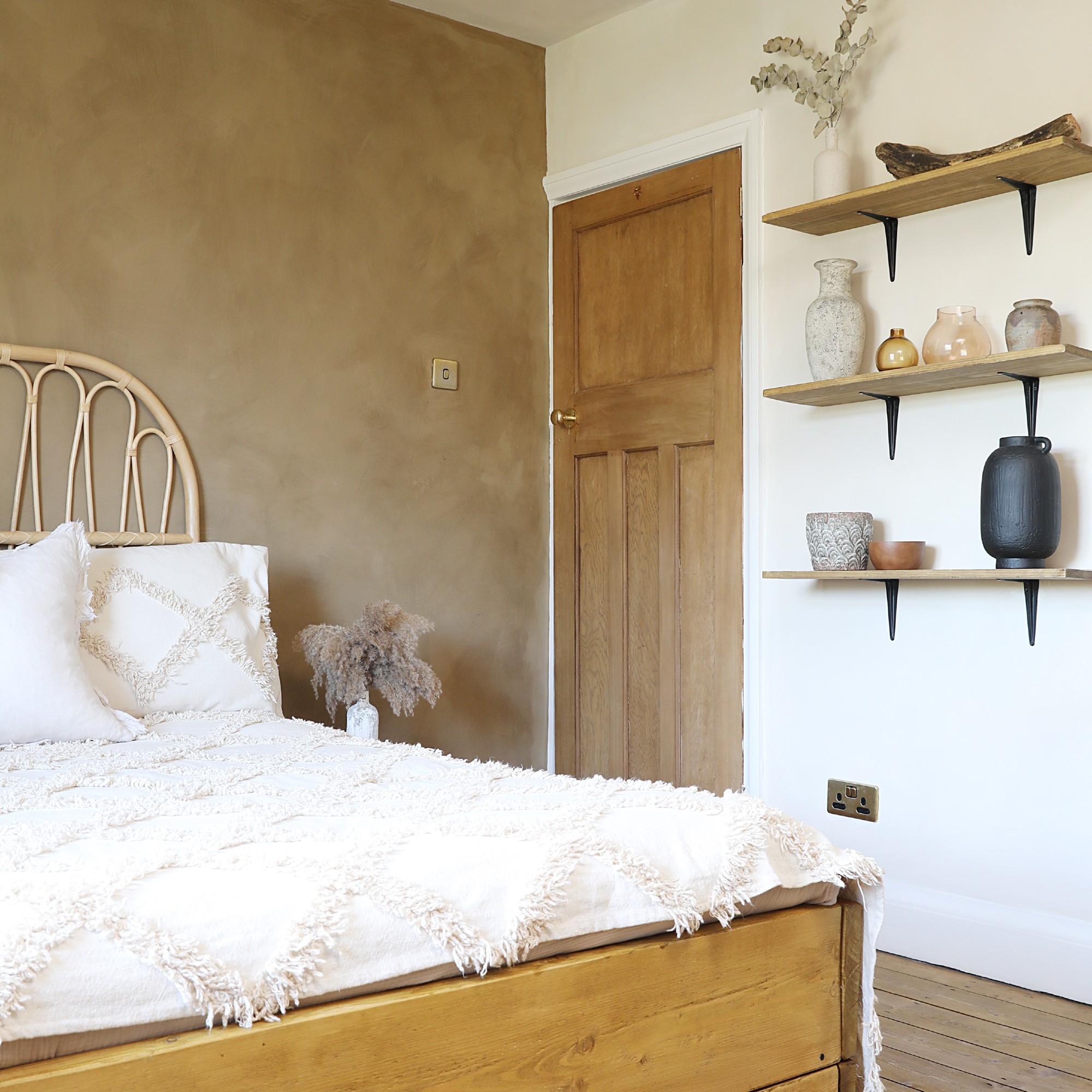 A neutral bedroom with a limewash-effect brown feature wall and floating shelves