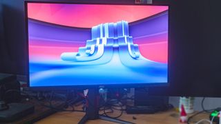 AOC GAMING Q27G4ZD monitor on desk with pink and blue rippled wallpaper.