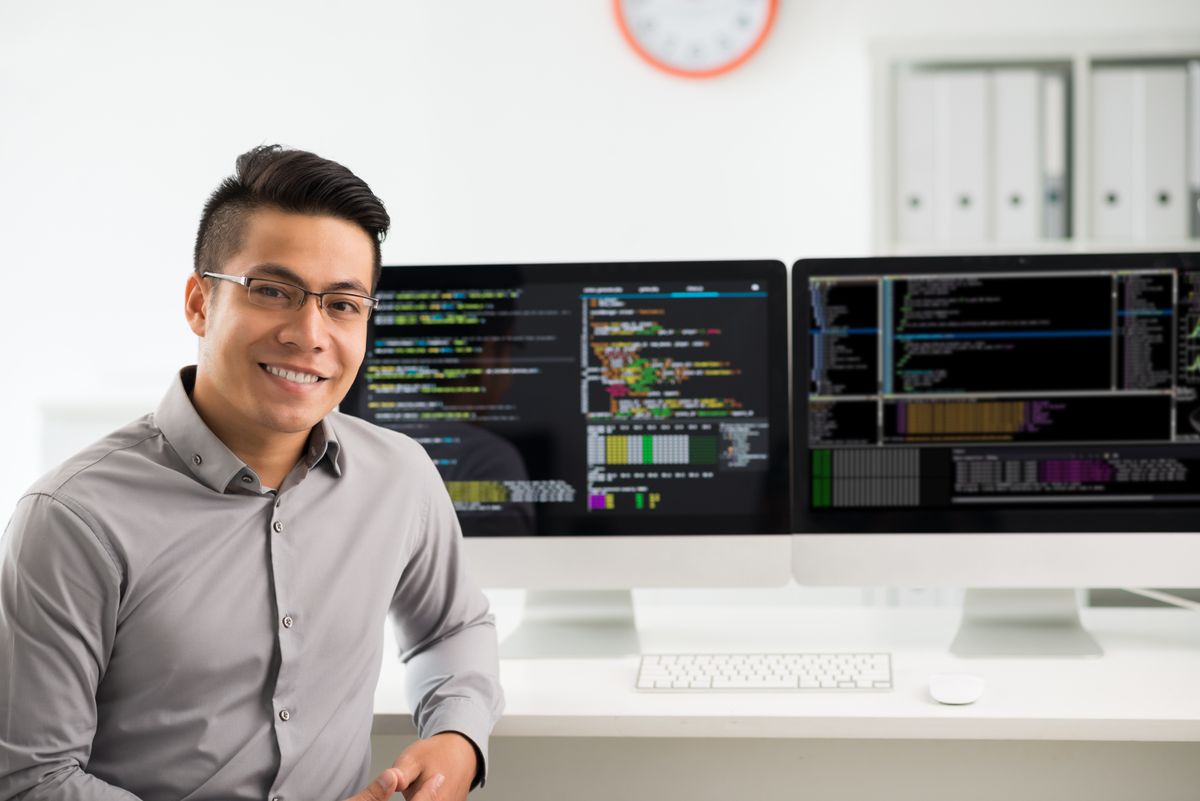 Man sitting in front of computer monitors with coding on them