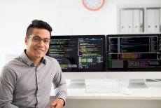 Man sitting in front of computer monitors with coding on them