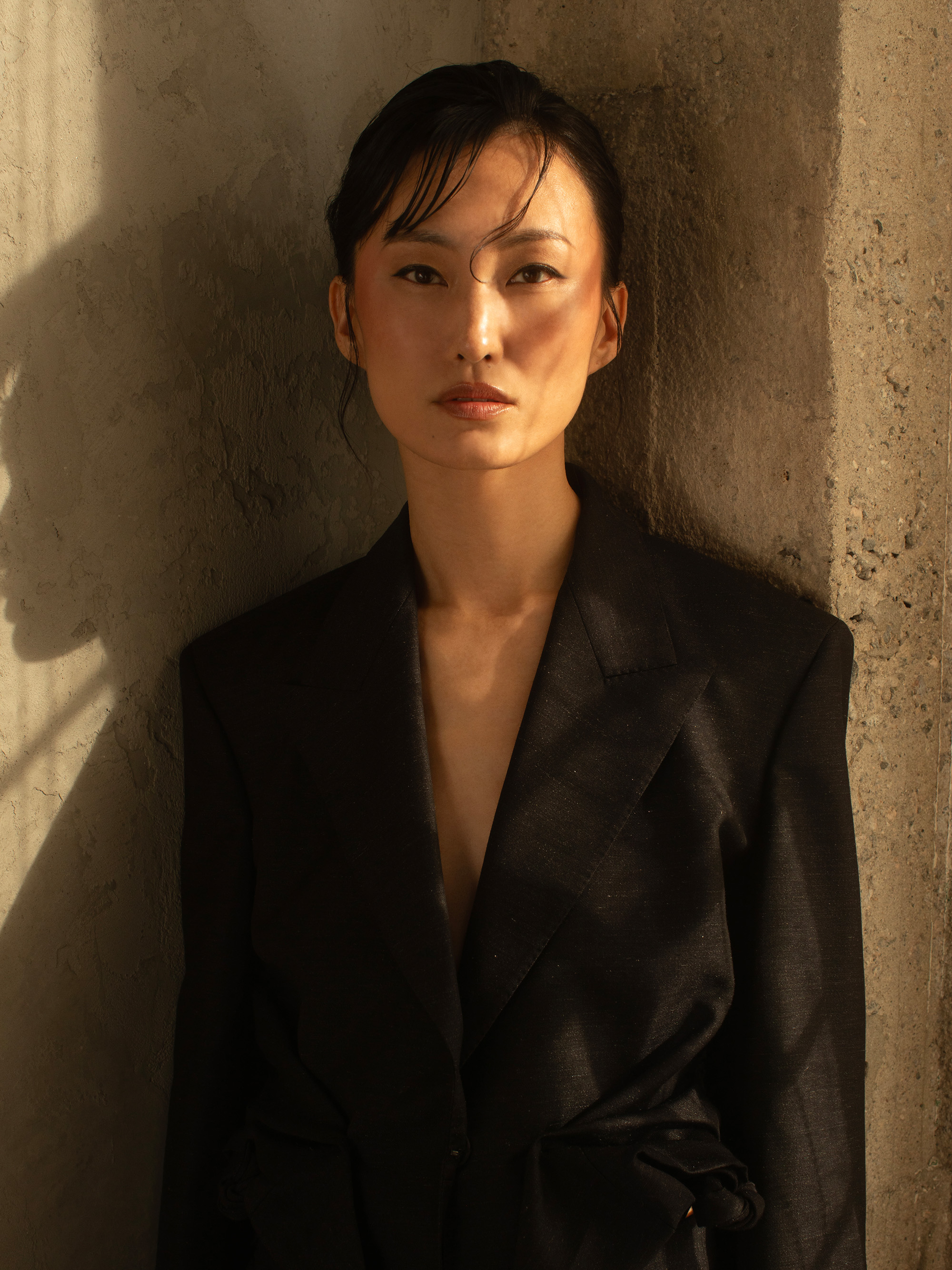 Actress Mari Yamamoto wears a black blazer standing against a concrete wall.