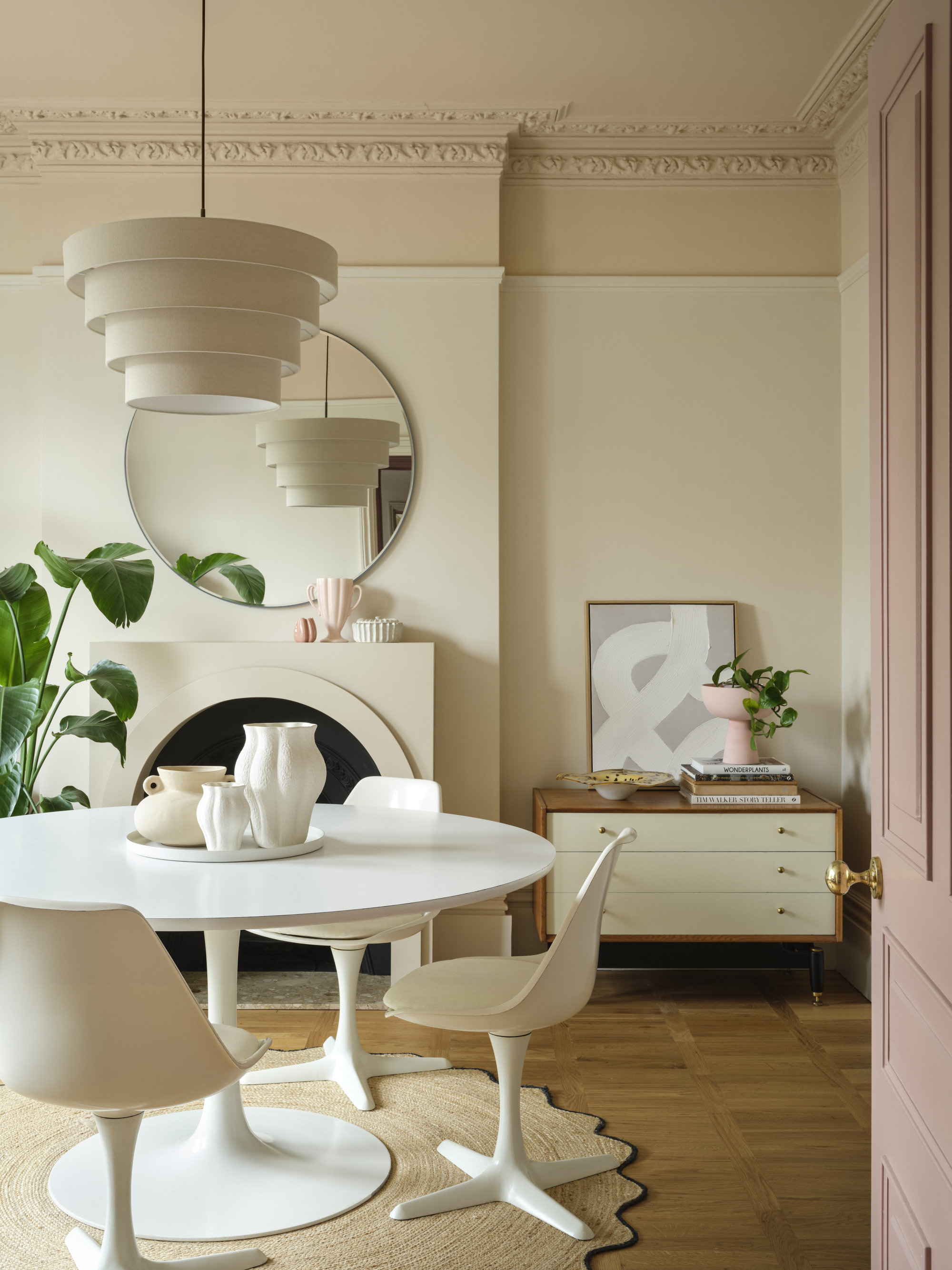 neutral dining room with tulip dining table and chairs, pendant light, crown molding, cabinet with artwork and vase and books, timber floors, and fireplace