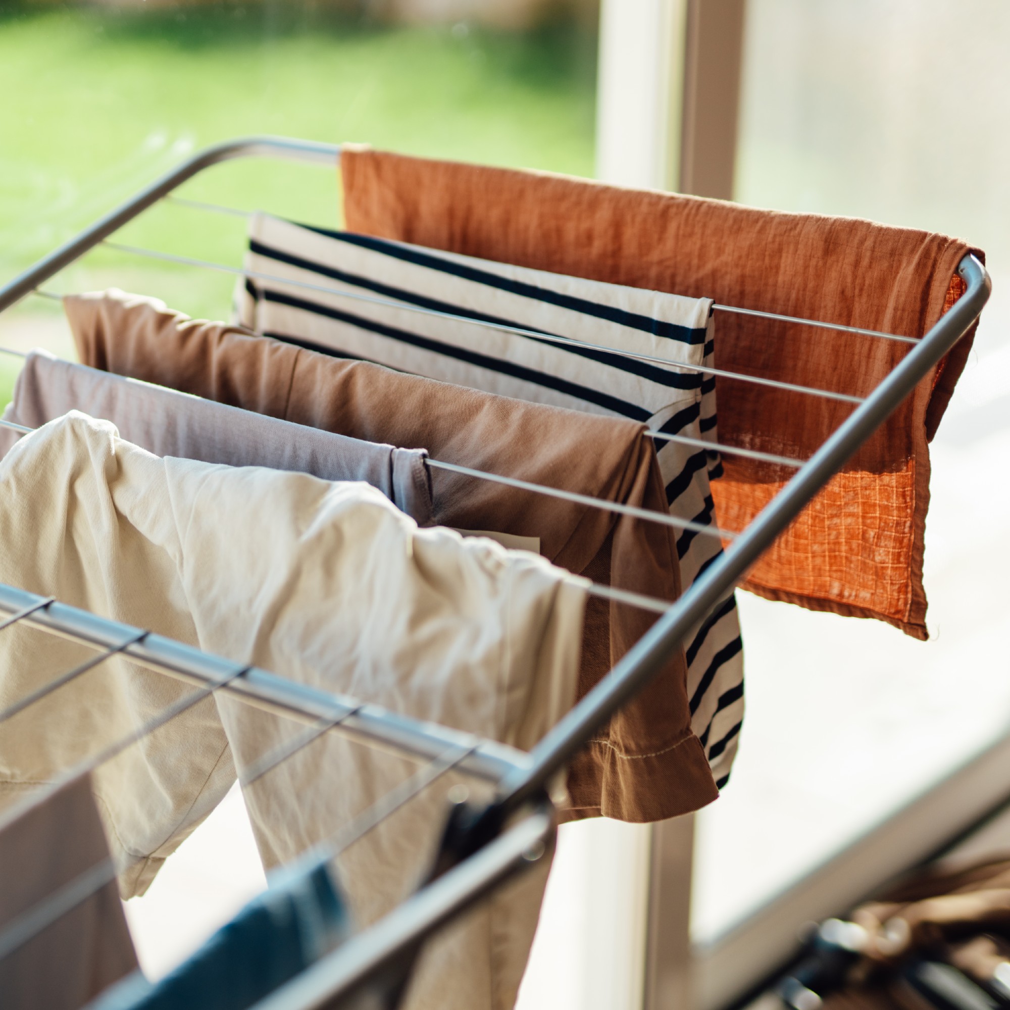 Clothes hanging on a clothes airer in a house, next to a window with views of the garden