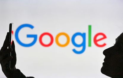 A woman holding a mobile phone in front of the Google logo displayed on a computer screen