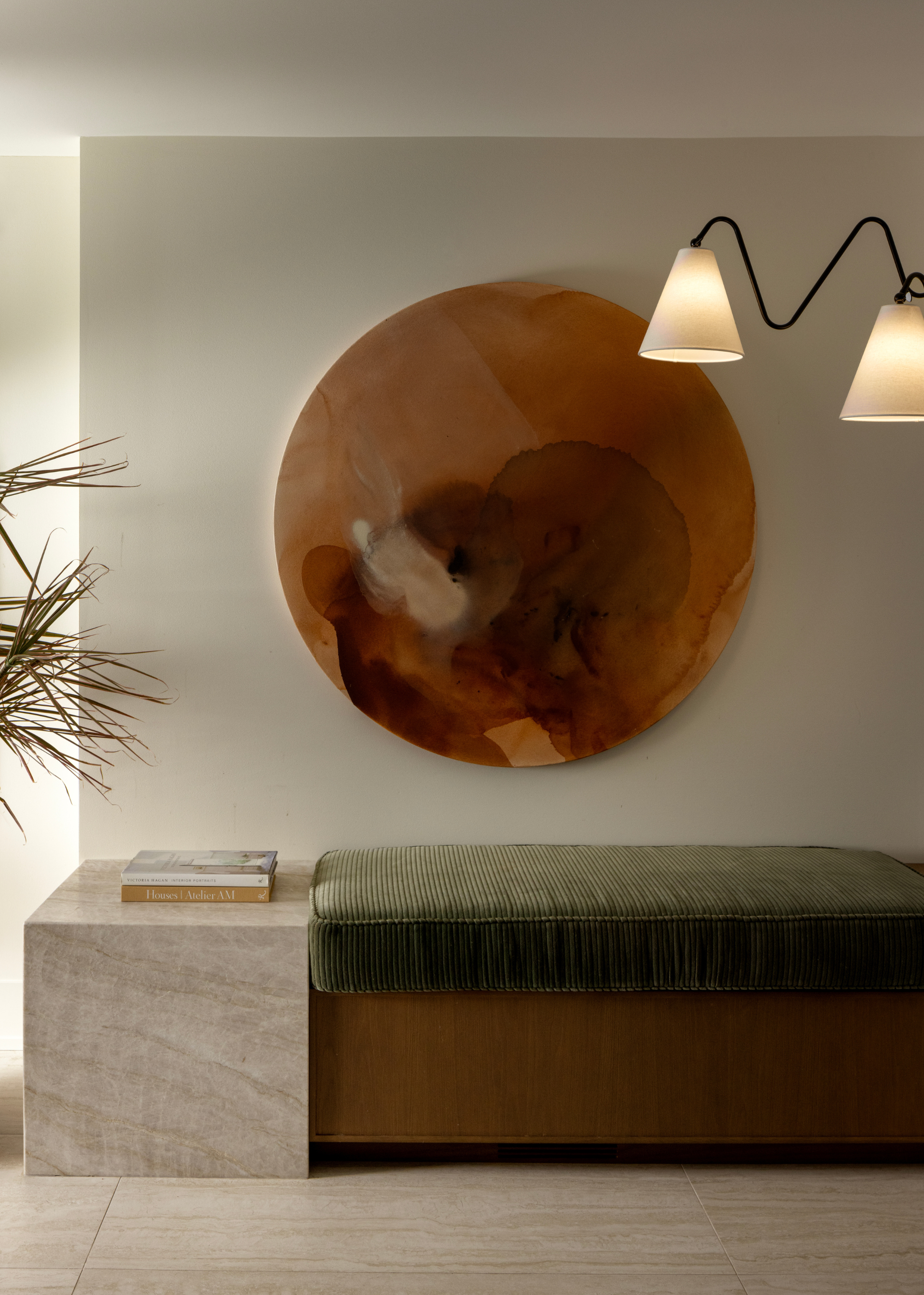 A green bench on a wood base by a stone side below a marbled round painting by bent wrought iron wall lamps
