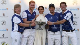 Prince Harry and Meghan Markle with polo players holding a cup