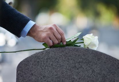 A person laying a flower on a gravestone 
