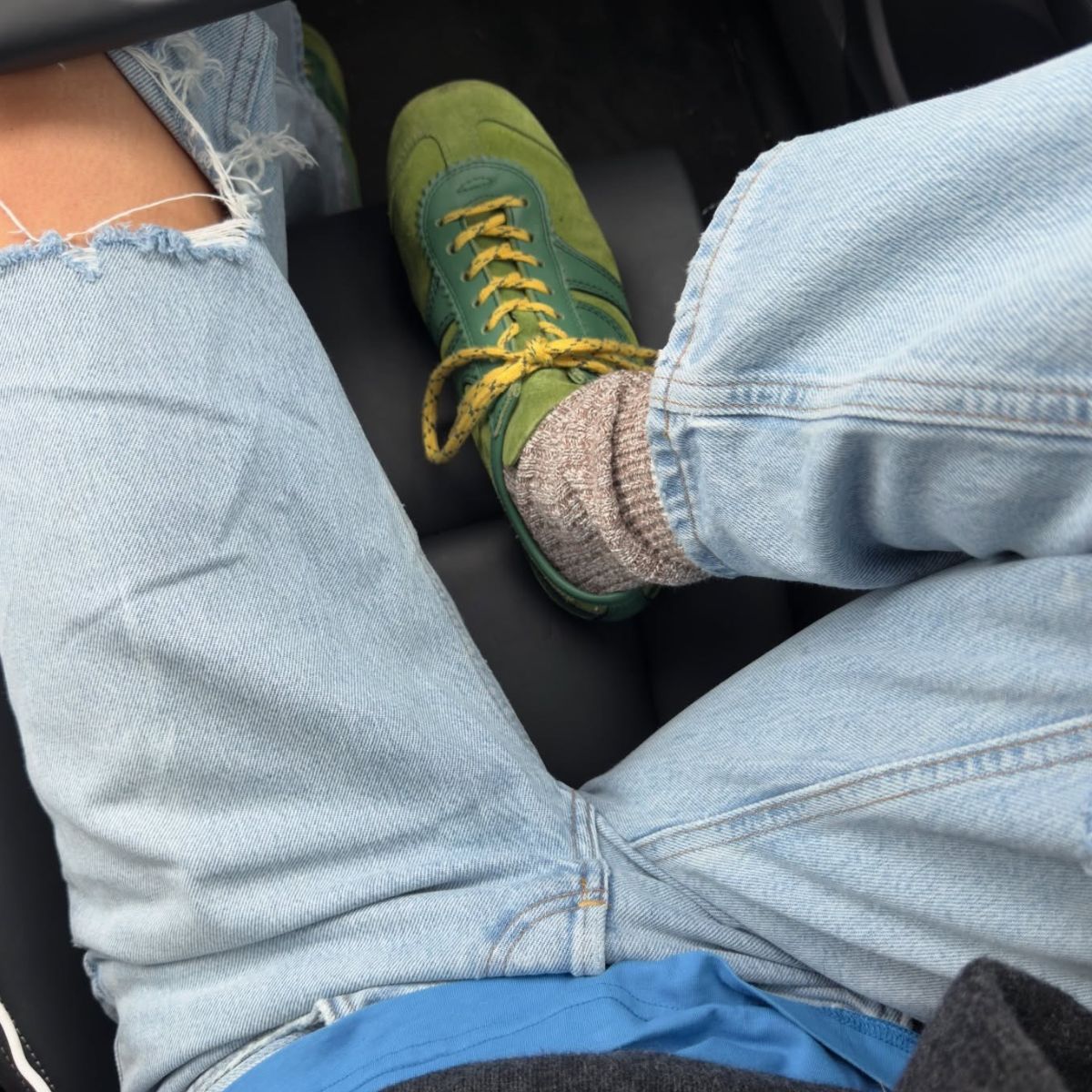 Fashion person smythsisters wears a trending trainer brand 2026. She wears green Dries Van Noten trainers. She wears them with blue ripped denim jeans, a blue tee and grey jumper. This image was recently taken from her Instagram. 
