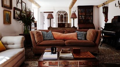 farmhouse living room with brown sofa, antique furniture and beamed ceiling