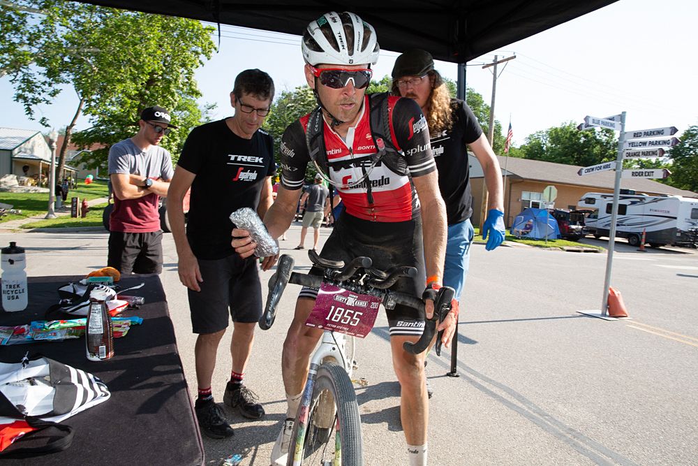 Peter Stetina grabs one extra sandwich on way out of the first checkpoint. Riders typically swapped their hydration packs with a new, pre-filled pack as mechanics triaged the bike for critical needs. A minute or two and riders were back on course.