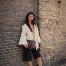 Woman wears white flowy blouse, black long shorts, tall square-toe boots, and a cute cluctch.