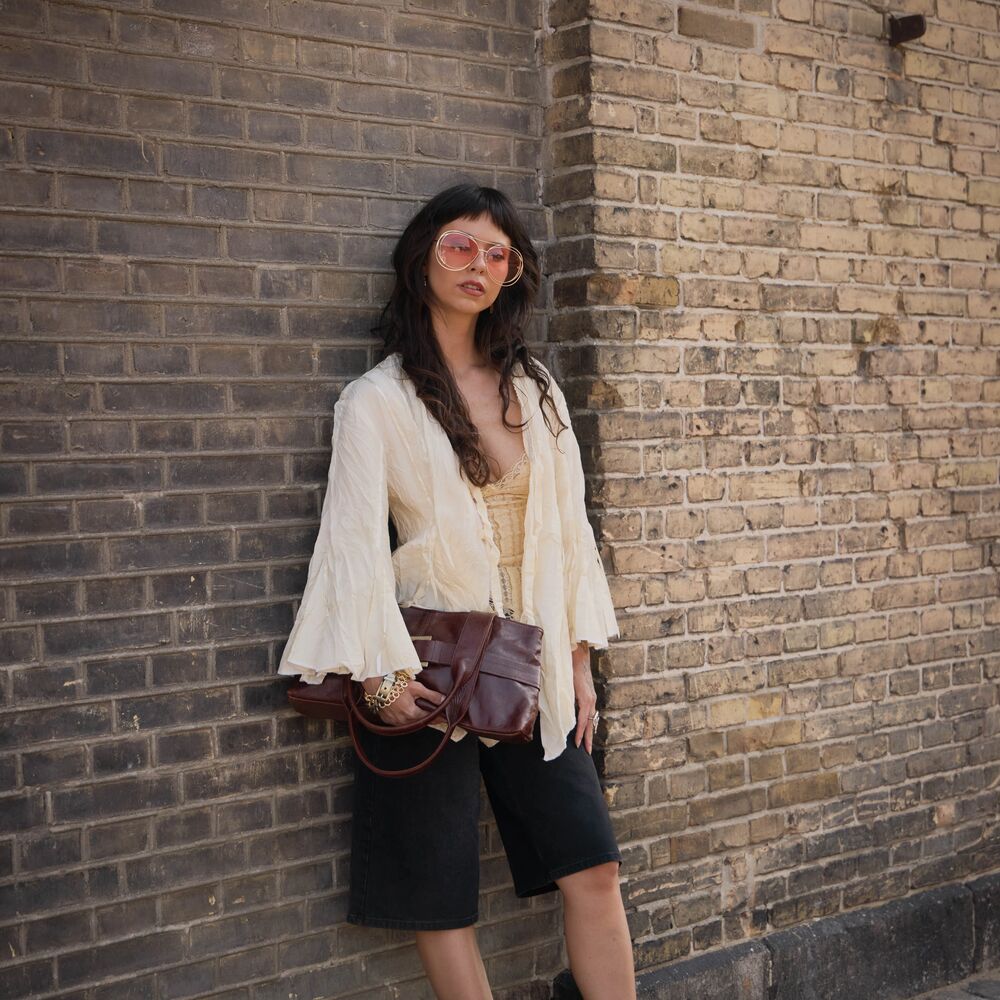 Woman wears white flowy blouse, black long shorts, tall square-toe boots, and a cute cluctch.