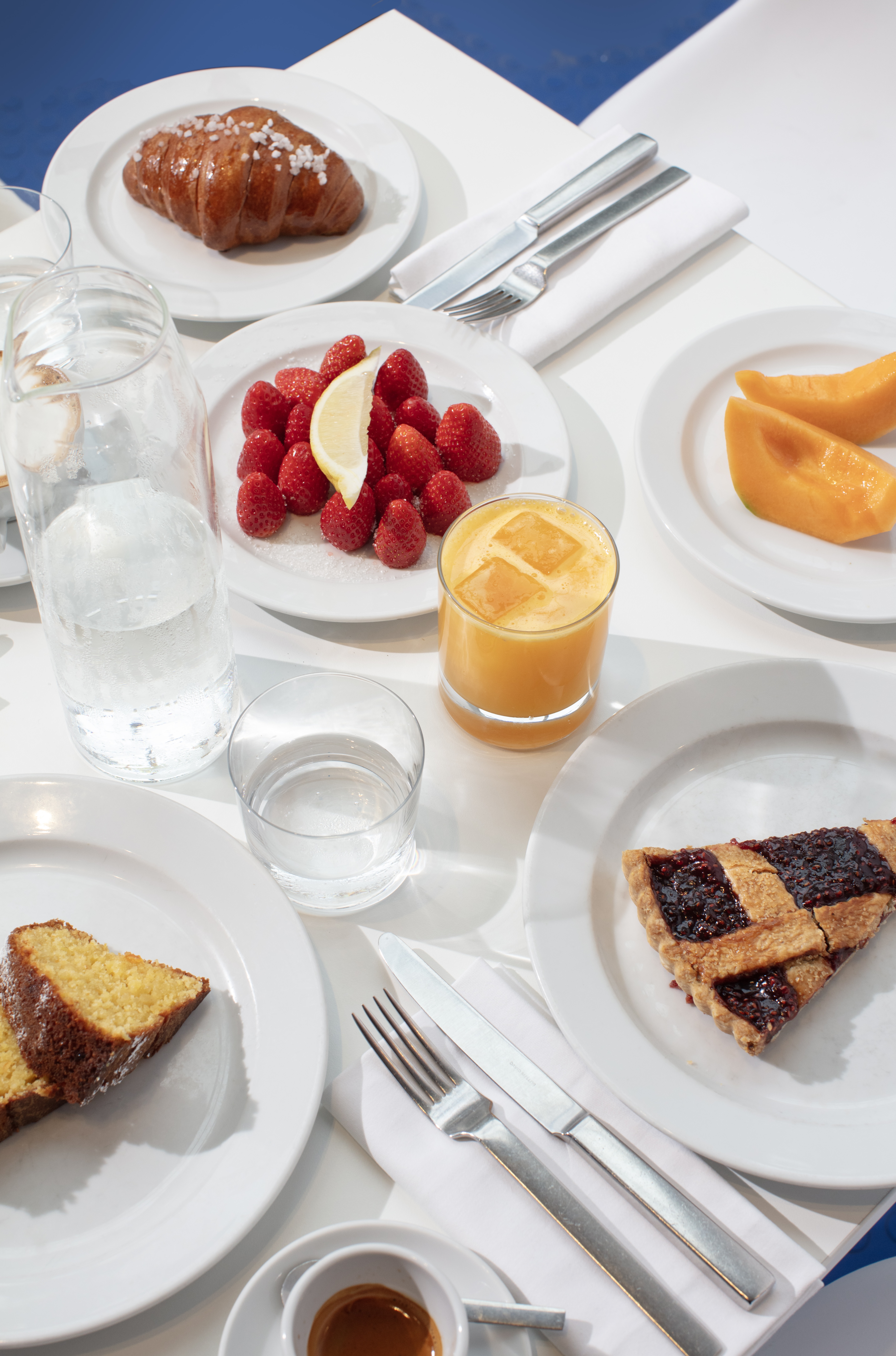 Pastries, fruit, fruit tarts and a glass of orange juice on a blue and white covered table
