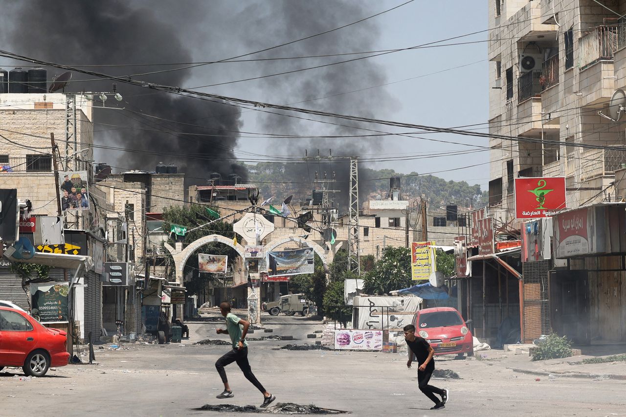 Two people run to take cover in Jenin in the occupied West Bank with smoke in the distance