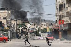 Two people run to take cover in Jenin in the occupied West Bank with smoke in the distance