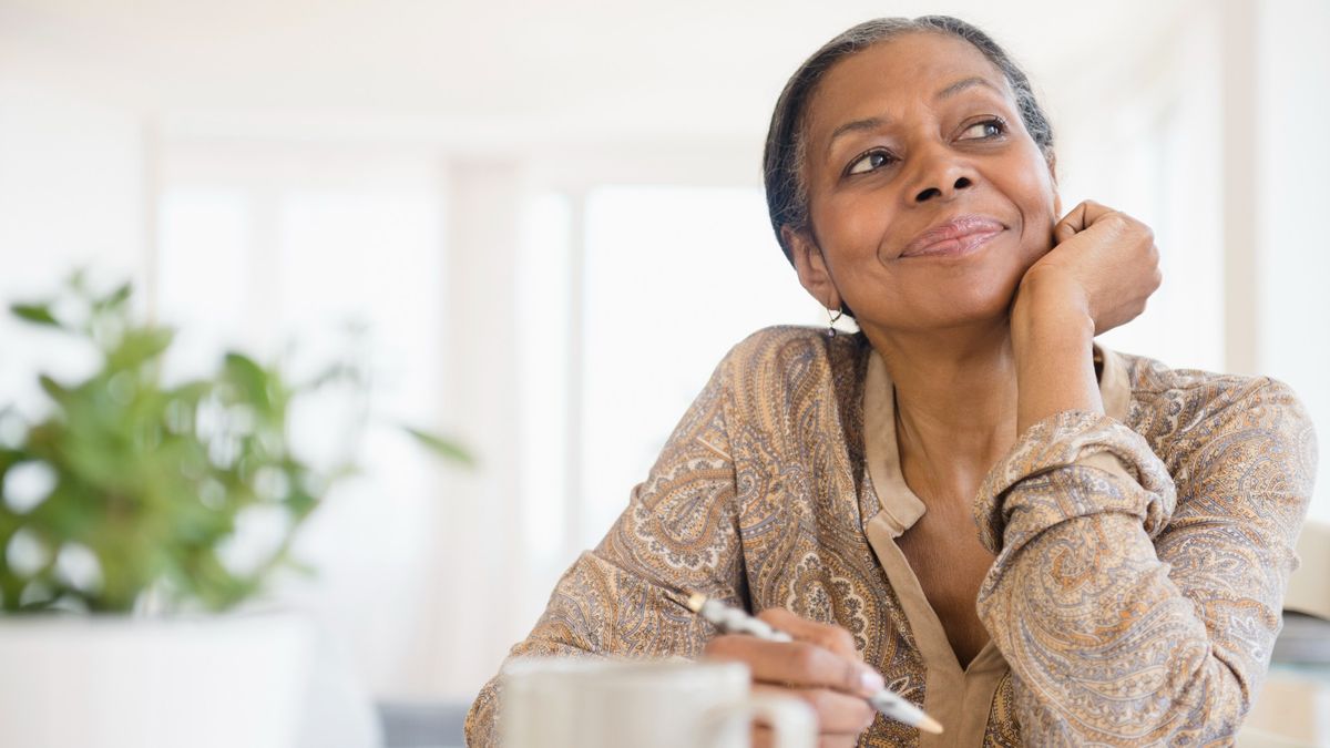 Mixed race woman writing at desk, looking off into the distance as if lost in thought.